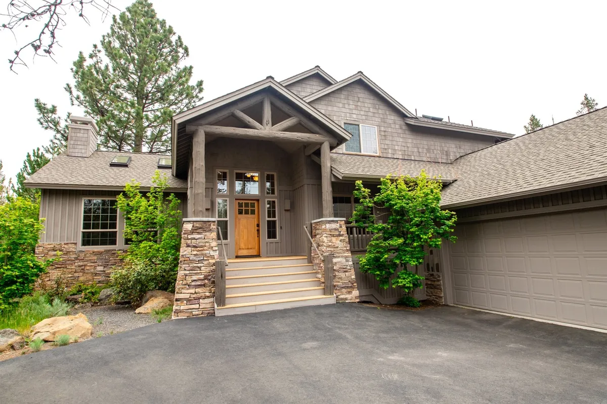 This exterior view shows the property’s entrance with a sturdy wooden door, stone features, garage, and surrounding greenery. The angle suggests a seamless blend between the home and the outdoor environment, perfect for gatherings or gearing up for an adventure.
