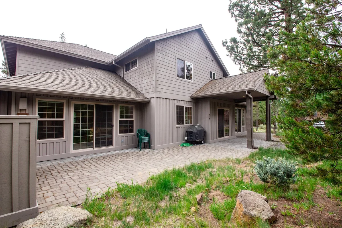 A welcoming patio area furnished with green chairs and a barbecue grill, nestled beside a landscaped garden and adjacent to the home’s facade. The scene suggests ample space for alfresco dining, relaxing with friends, or unwinding after outdoor adventures.