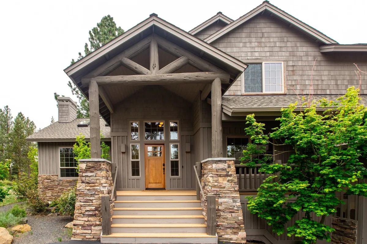 This exterior image shows the inviting front porch of the home, featuring a sturdy wooden door framed by classic stone pillars and surrounded by lush greenery. The scene suggests a welcoming entry and a tranquil environment that is ideal for both morning coffee and evening relaxation after a day of family activities.