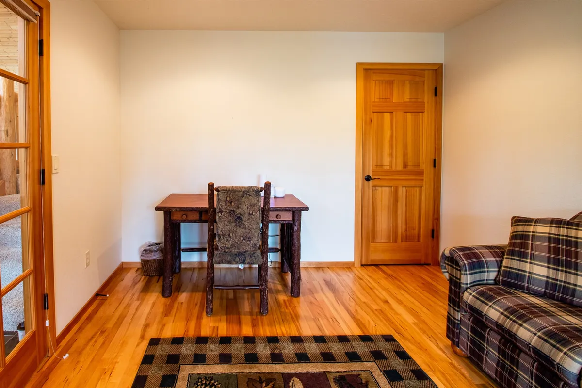 A dedicated workspace with a wooden desk and a plaid sofa, positioned near a doorway and bathed in soft sunlight. The atmosphere is both functional and cozy, suitable for remote work or as an extra guest room.