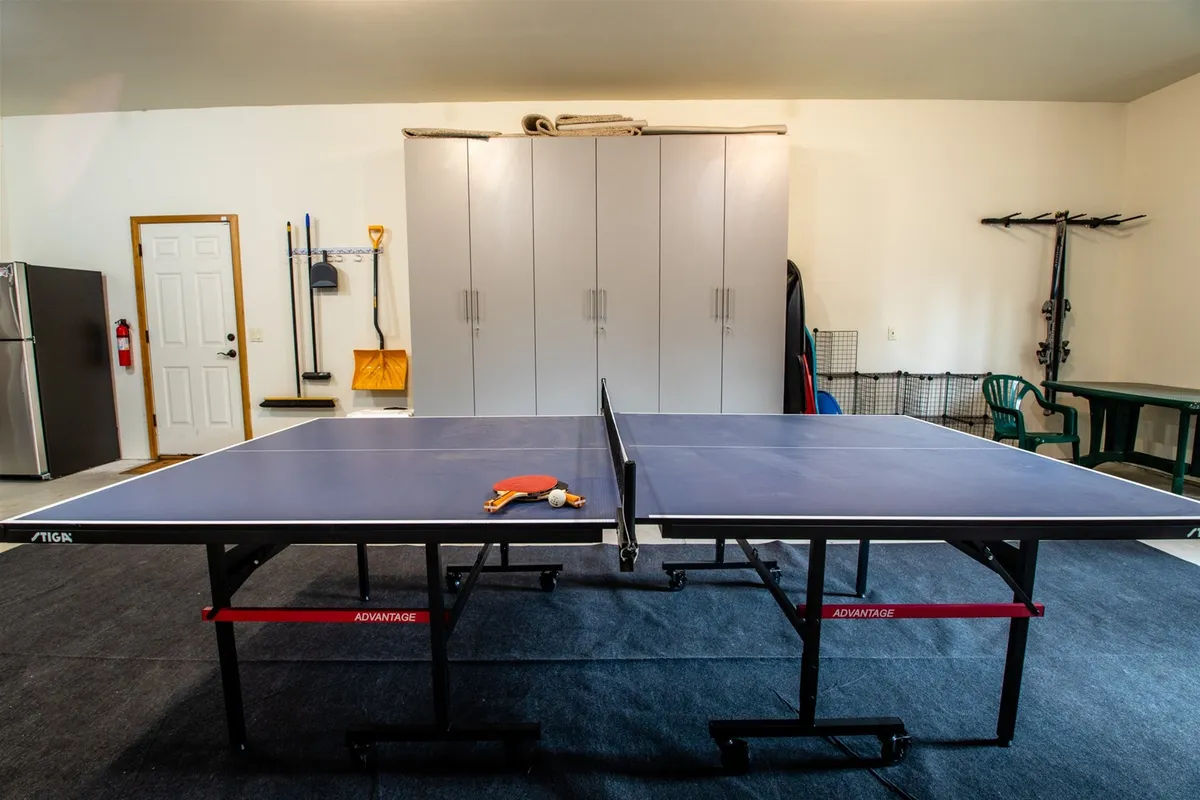 A dedicated recreation room with a ping pong table, storage cabinets, and a green chair. The space is playful, bright, and ready for friendly games or casual gatherings.