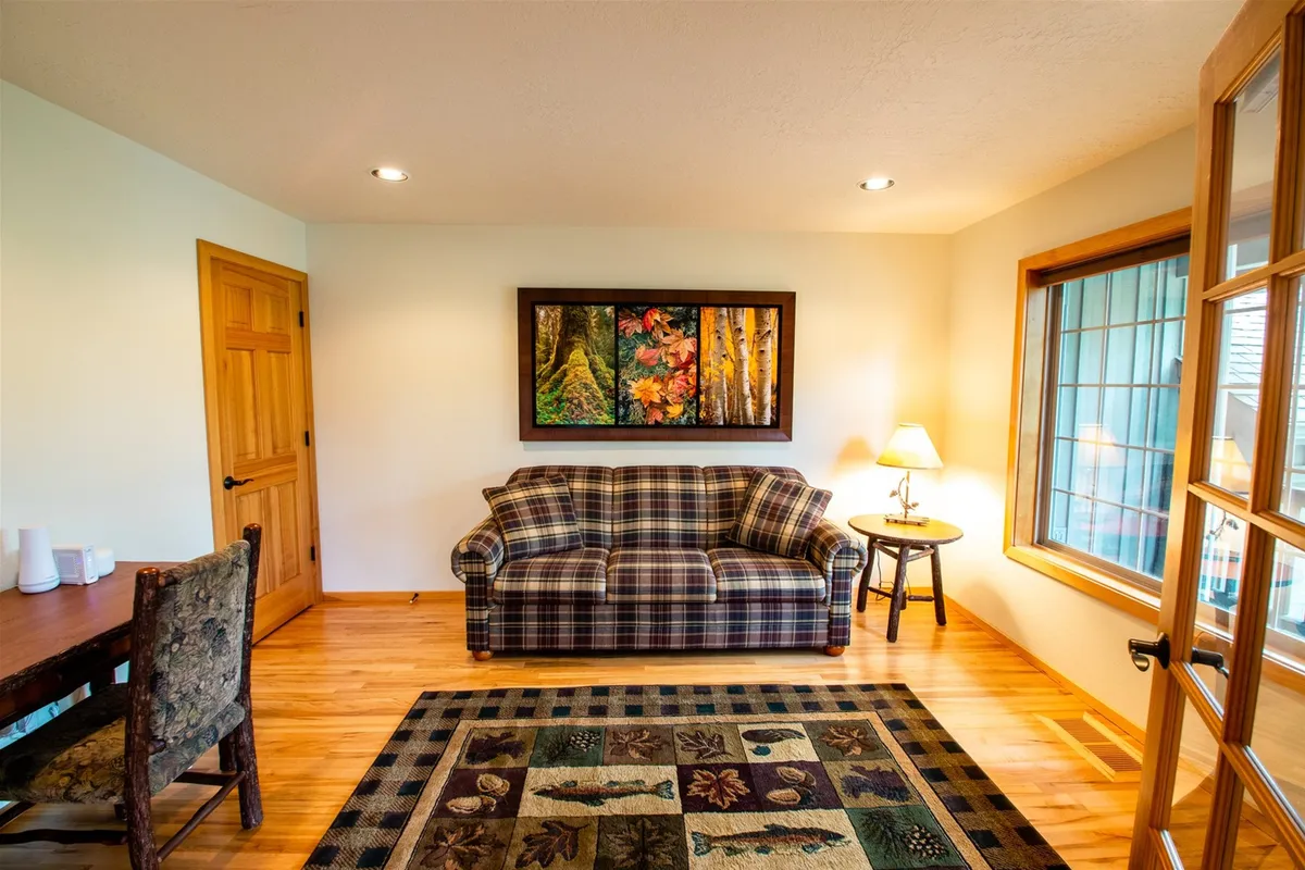A cozy living room featuring a plaid sofa, nature-themed artwork, a wooden coffee table, and a decorative lamp. The arrangement encourages guests to relax, socialize, enjoy coffee, or play games together in a warm, inviting space.
