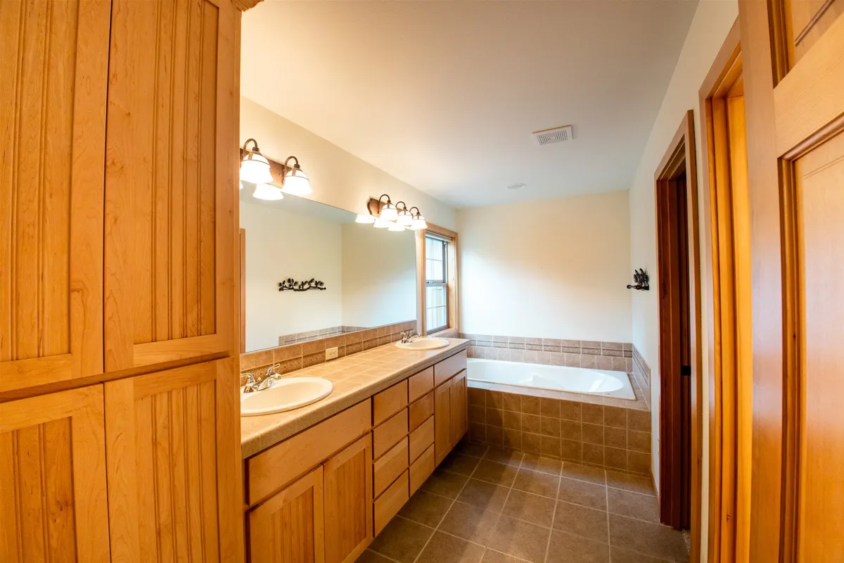 A serene bathroom with a modern vanity, large mirror, inviting bathtub, and a window that fills the space with light. The setting is calm and spa-like, emphasizing relaxation and self-care.