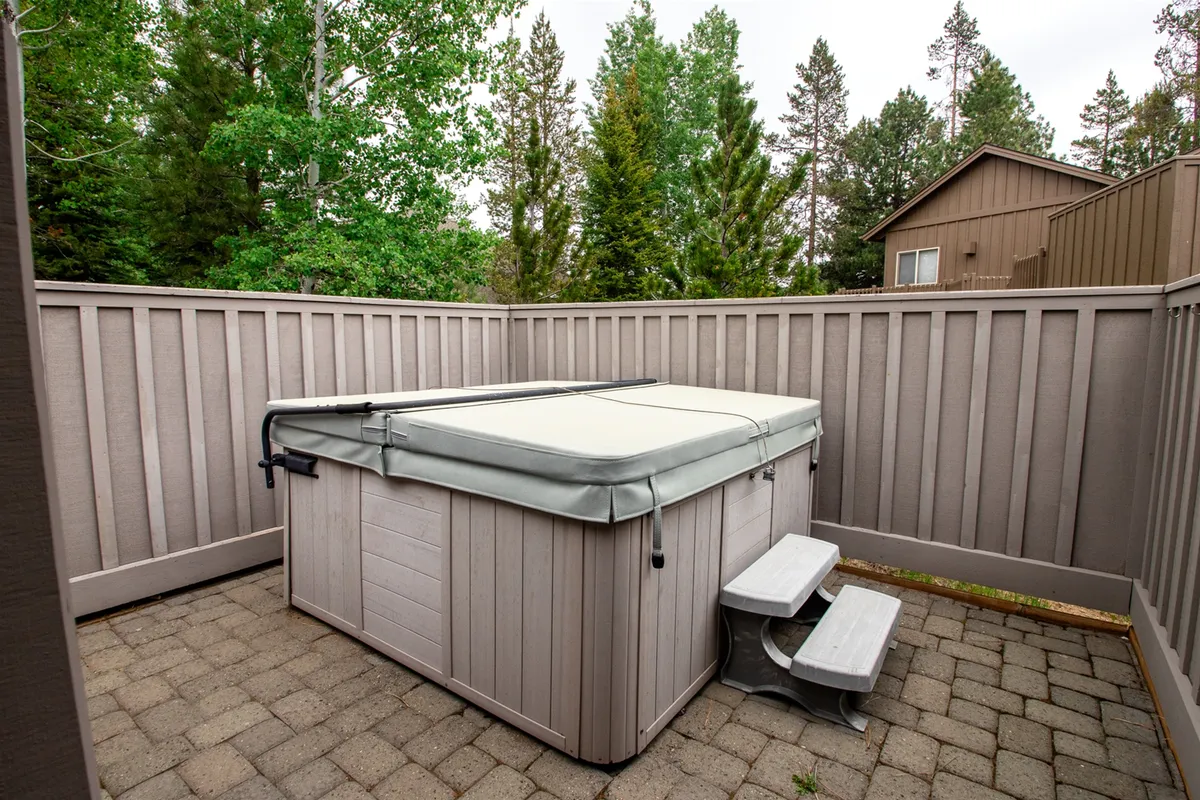 An exterior shot of a bubbling hot tub surrounded by stone pavers and lush greenery, offering a sense of privacy and tranquility. The hot tub is inviting, perfect for post-adventure relaxation under the stars or during a crisp morning.