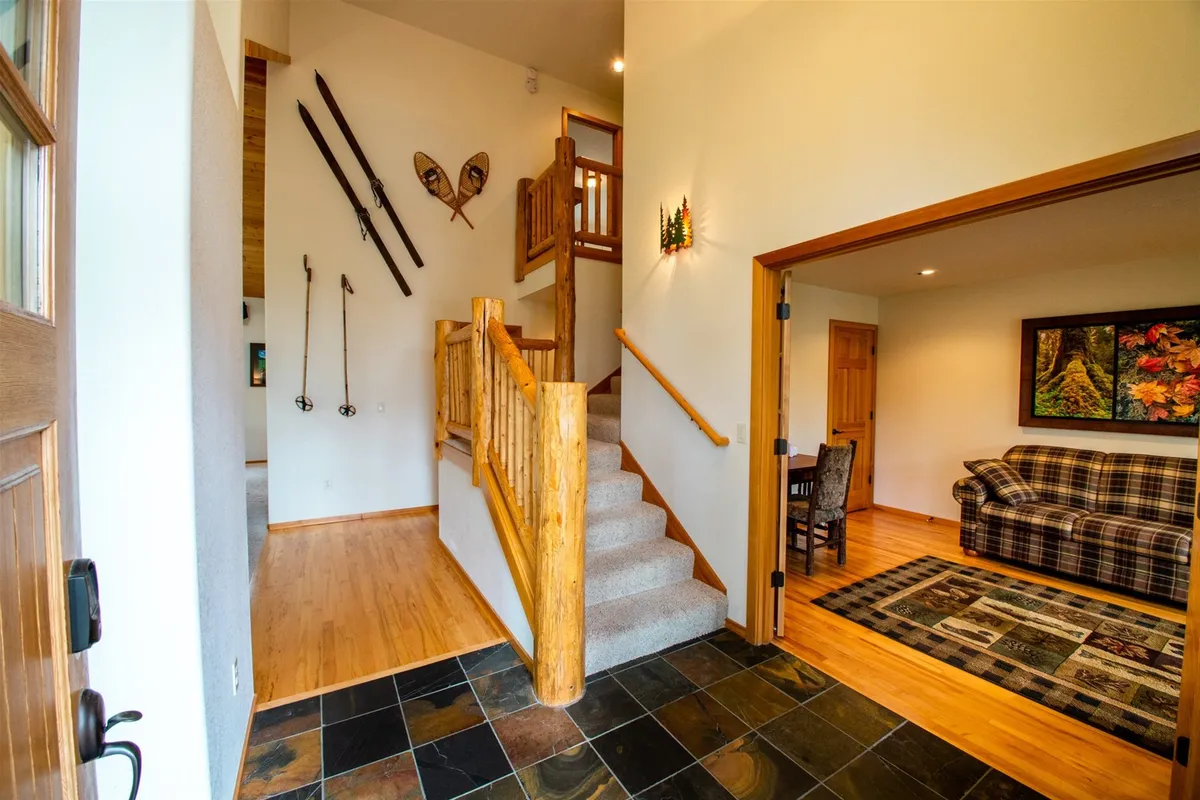 This warm, inviting living space features a plaid couch, cozy wooden decor, a staircase, and local artwork on the wall. It serves as both a relaxing lounge and a display area for regional artistry, reflecting the inspiration and serenity mentioned in the section.