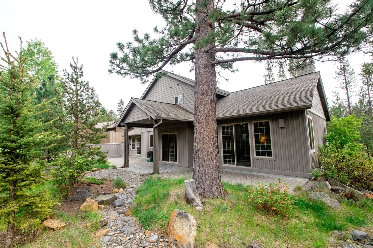An exterior view highlighting a large pine tree, a charming stone pathway leading to the house facade, and a peaceful outdoor setting. The image conveys the serene, spacious environment that surrounds the property and invites exploration and outdoor play.