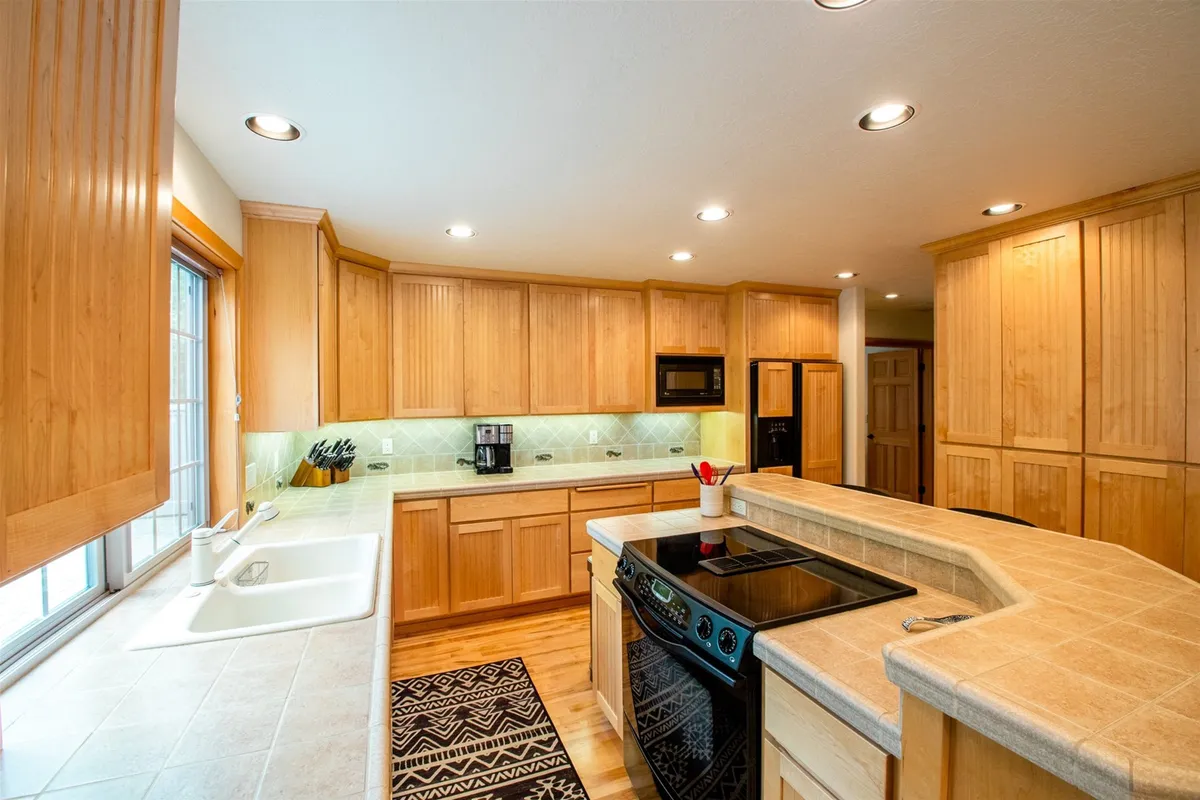 The kitchen is showcased here, with a central island, stainless steel appliances, warm wood cabinetry, and abundant natural light from the windows. The layout is both functional and inviting, encouraging group cooking and casual snacking.