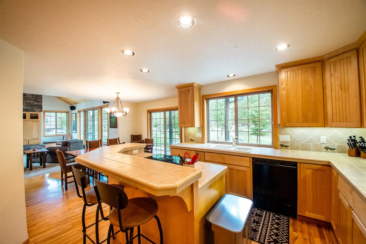 A spacious, warmly lit kitchen with a prominent island, wood cabinetry, and large windows revealing scenic outdoor views. The setup is perfectly suited for group cooking, entertaining, and casual gatherings, with ample space for friends to interact and host culinary nights.